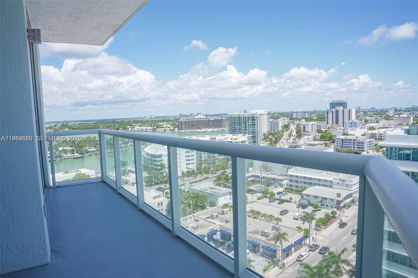 A high-rise balcony with a glass railing overlooks a city street and a bay — 6515 Collins Ave # 1709, Miami Beach FL 33141, MIAMI BEACH, FL