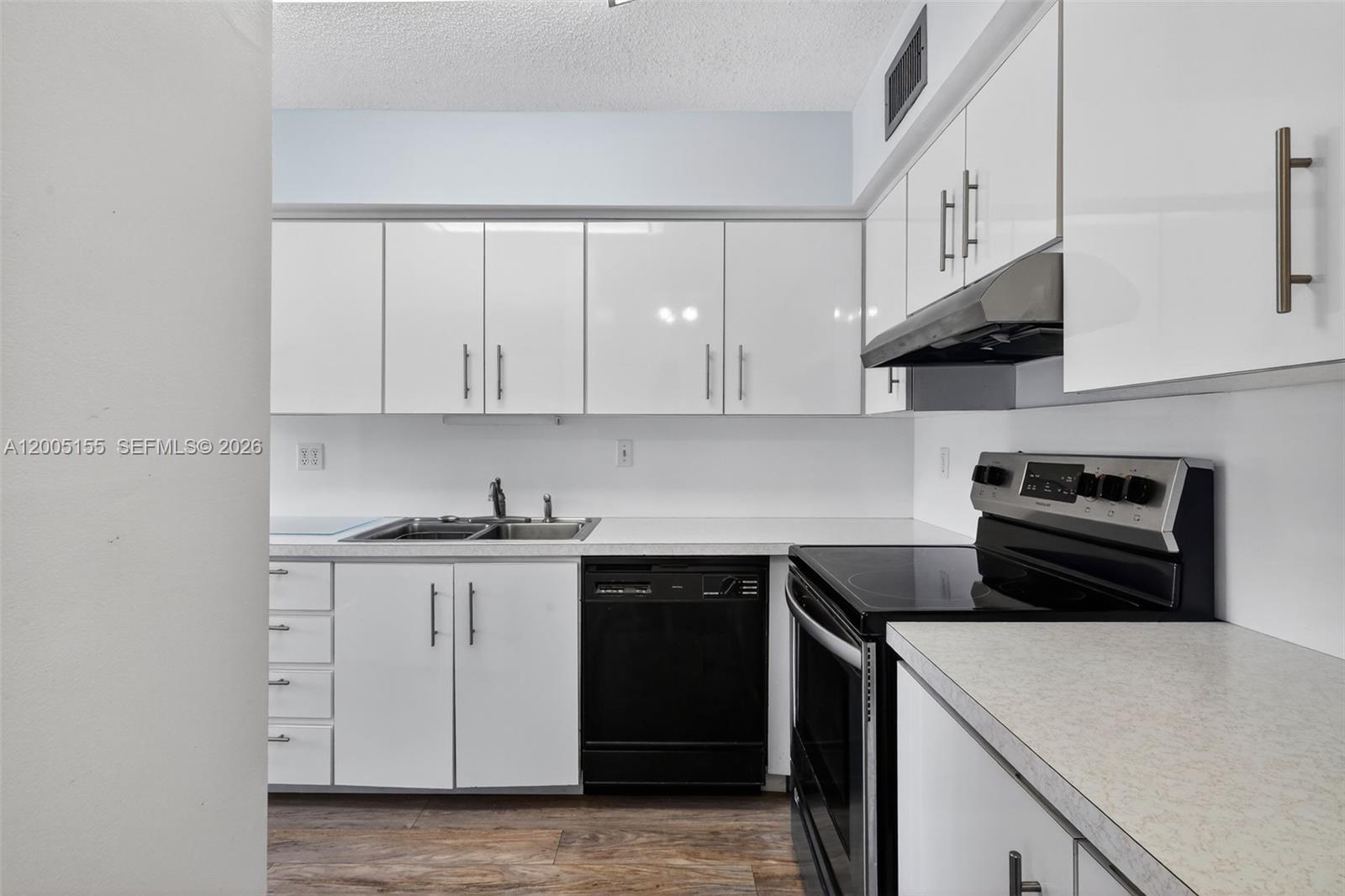 A kitchen features white cabinets, a black dishwasher, a black stove, and light countertops — 13950 Via Flora # D, Delray Beach FL 33484, DELRAY BEACH, FL