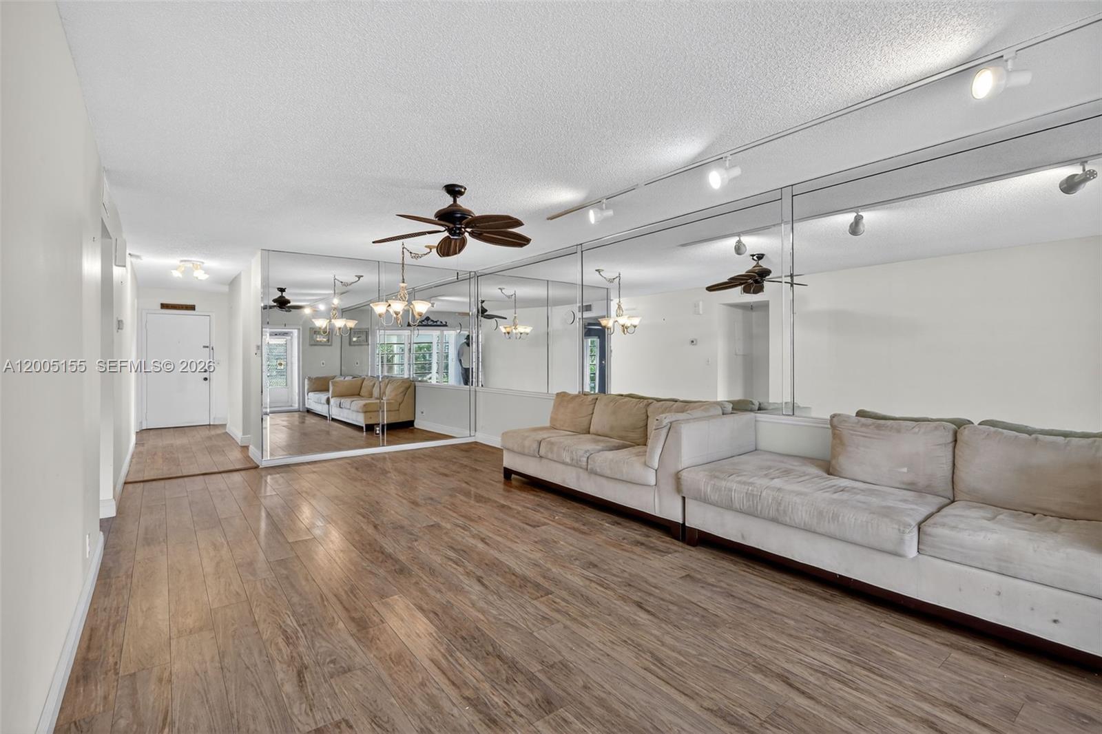 A living room features wood-look flooring, a large mirrored wall, and a beige sectional sofa — 13950 Via Flora # D, Delray Beach FL 33484, DELRAY BEACH, FL