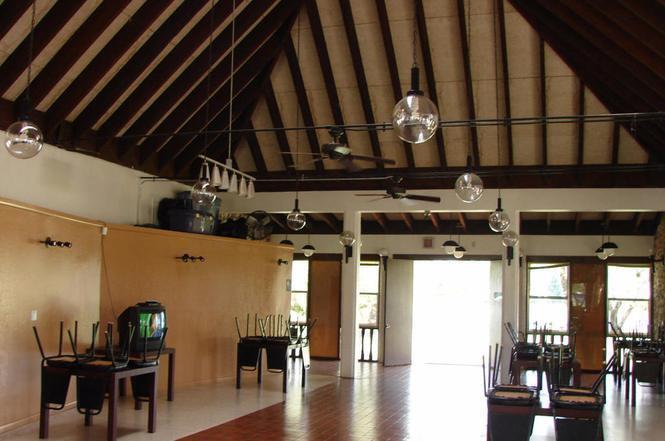 A spacious room with a vaulted wood-beamed ceiling, pendant lighting, and tables with stacked chairs — 725 S Willow Street, Clewiston FL 33440, CLEWISTON, FL