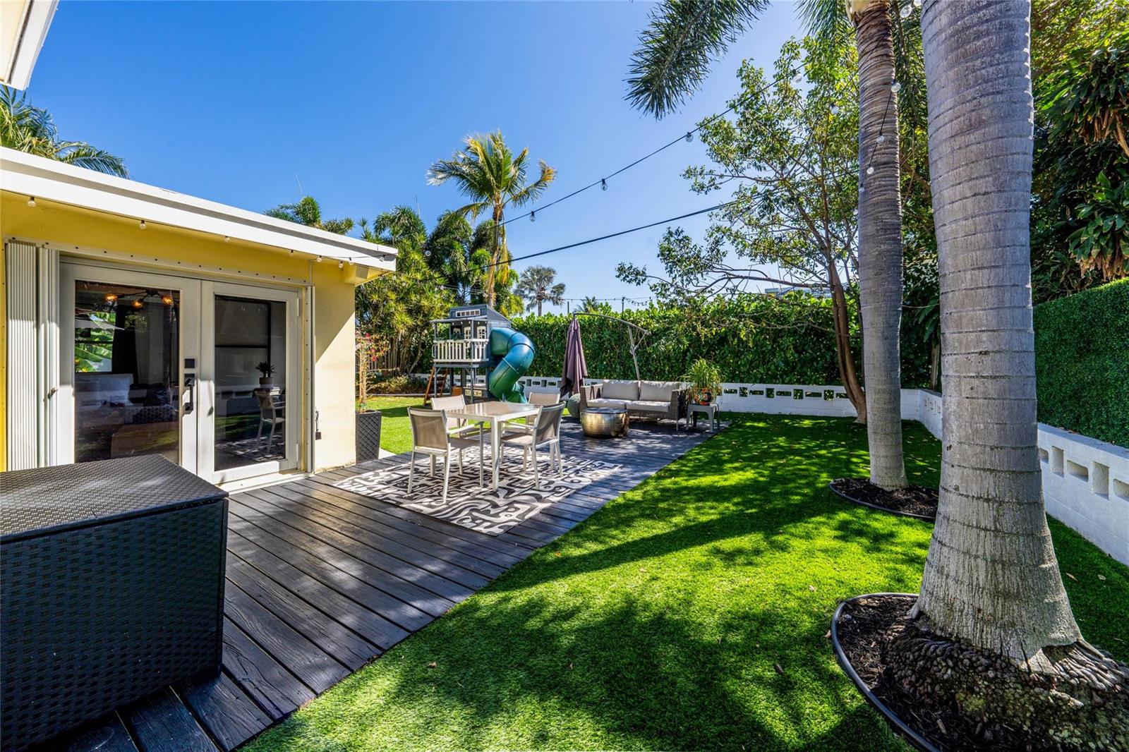 A backyard features a wooden deck with dining furniture, a play set, and palm trees — 2630 NE 25th Street, Lighthouse Point FL 33064, LIGHTHOUSE POINT, FL