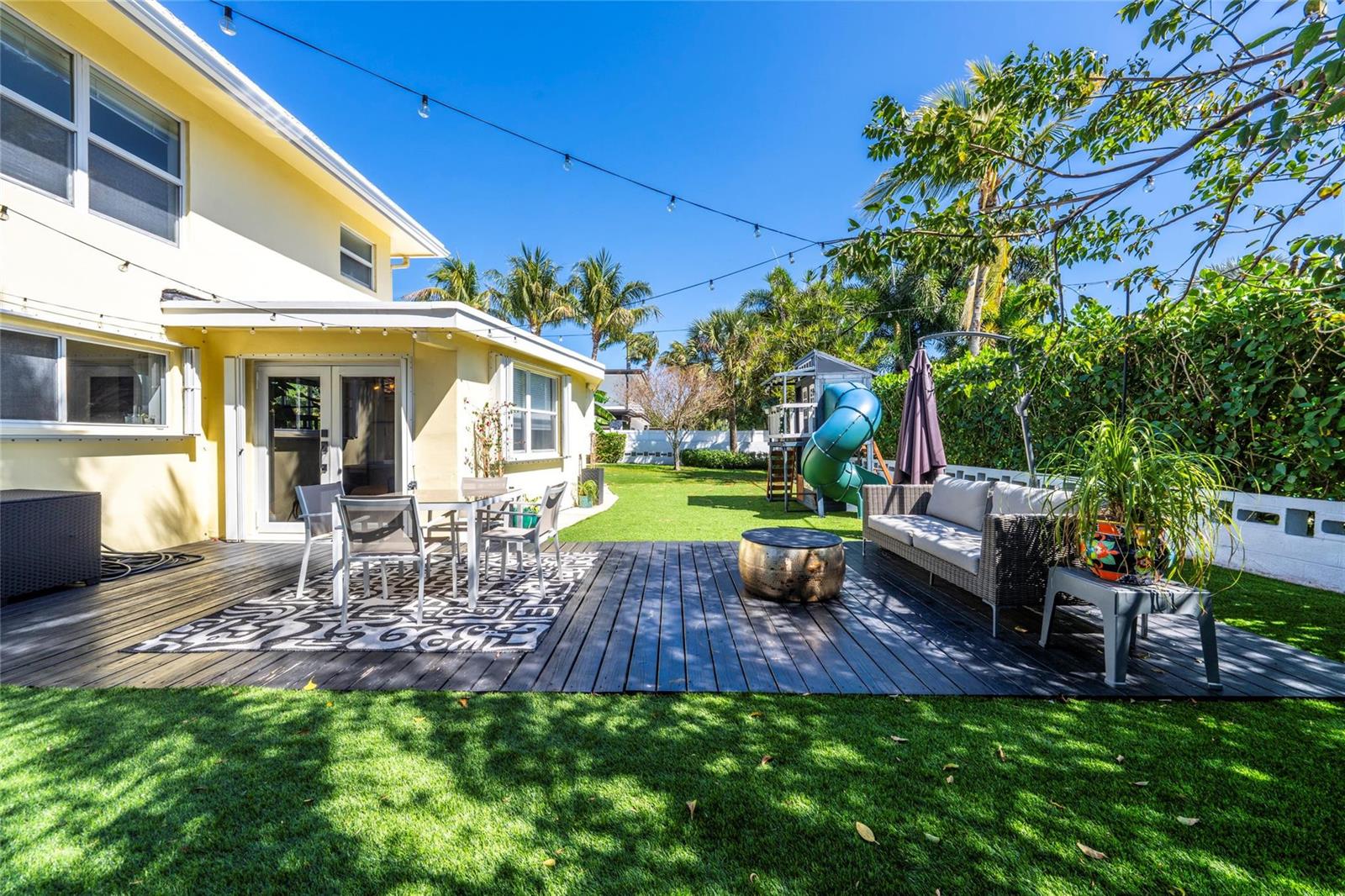 A backyard features a wooden deck with outdoor furniture, a play set, and artificial turf — 2630 NE 25th Street, Lighthouse Point FL 33064, LIGHTHOUSE POINT, FL
