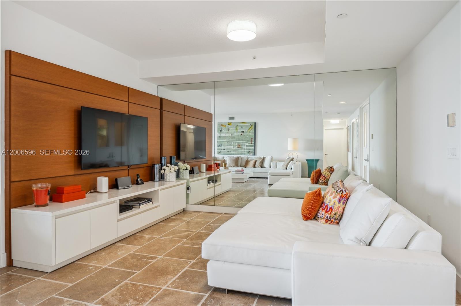 A living room features a white sectional sofa, a wood-paneled media wall, and mirrored walls — 747 Crandon Blvd, Key Biscayne FL 33149, KEY BISCAYNE, FL