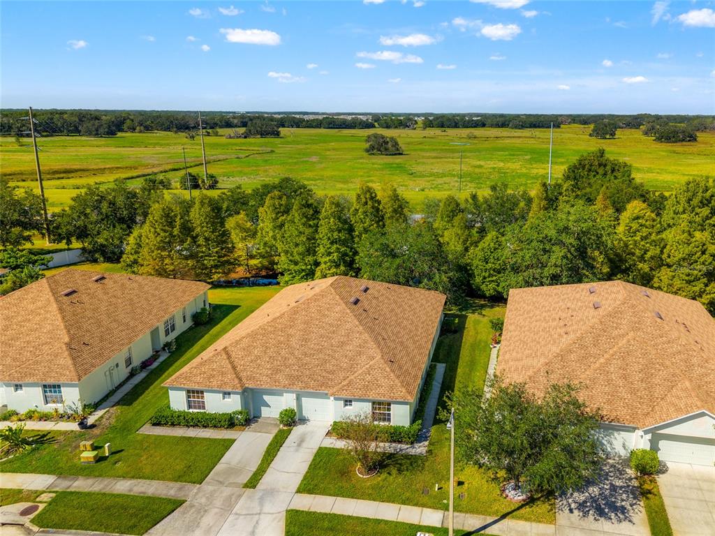 An aerial view shows three suburban houses with brown roofs overlooking a large grassy field — 5727 AUTUMN SHIRE DRIVE, ZEPHYRHILLS, FL