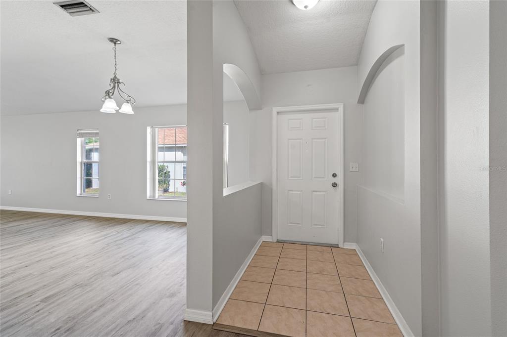 An entryway with tiled flooring leads to a white front door and an adjacent living area — 5727 AUTUMN SHIRE DRIVE, ZEPHYRHILLS, FL