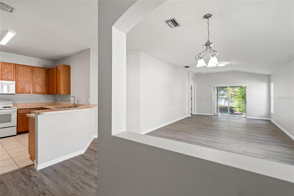 A view from a kitchen looking into an open-concept living area with wood-look flooring — 5727 AUTUMN SHIRE DRIVE, ZEPHYRHILLS, FL