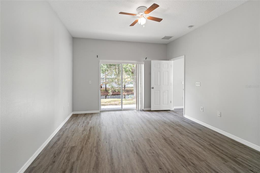 An empty room with gray walls, wood-look flooring, a ceiling fan, and a sliding glass door — 5727 AUTUMN SHIRE DRIVE, ZEPHYRHILLS, FL