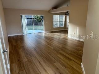 An empty living room features light wood-look flooring, a vaulted ceiling, and a sliding glass door — 2023 GREEN JUNIPER LANE, BRANDON, FL