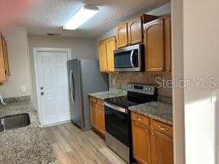 A kitchen features wood cabinets, granite countertops, stainless steel appliances, and light-colored flooring — 2023 GREEN JUNIPER LANE, BRANDON, FL