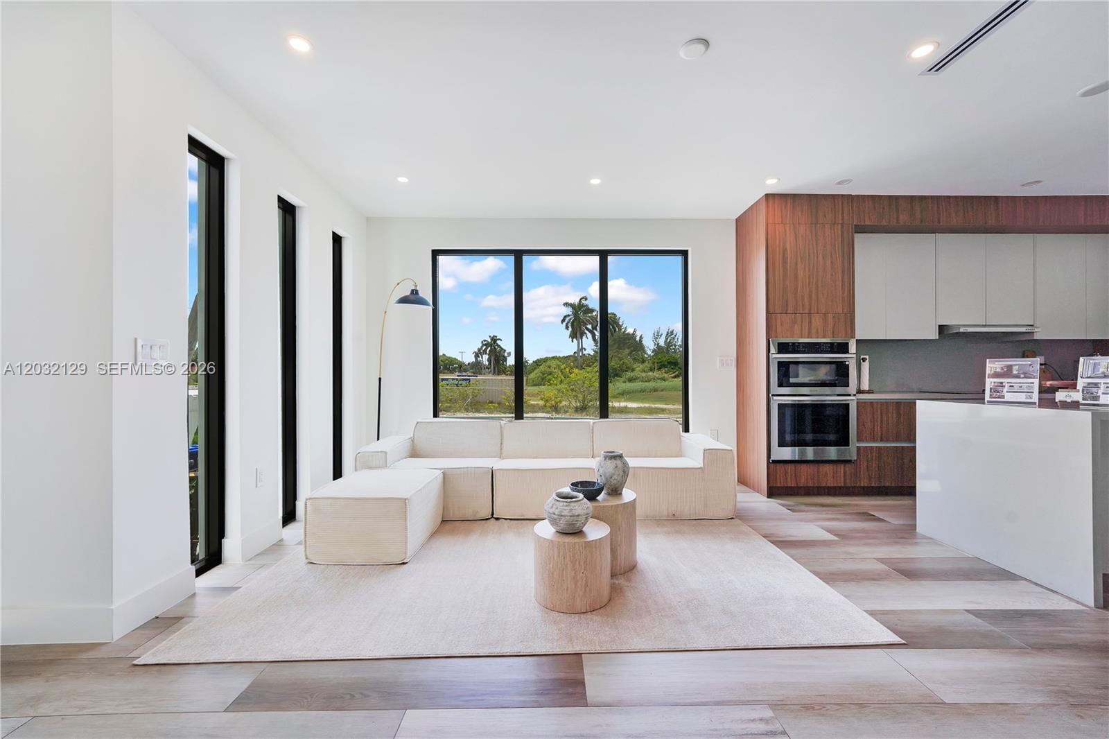 A modern living room features a white sectional sofa, wood-toned cabinetry, and large floor-to-ceiling windows — 2665 Johnson St, Hollywood FL 33020, HOLLYWOOD, FL