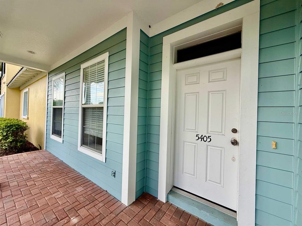 A white front door with the number 5405 sits on a brick porch with blue siding — 5405 CAFREY PLACE, APOLLO BEACH, FL