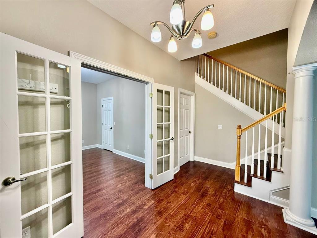 An entryway features wood-look flooring, a staircase with white railings, and French doors leading inside — 5405 CAFREY PLACE, APOLLO BEACH, FL