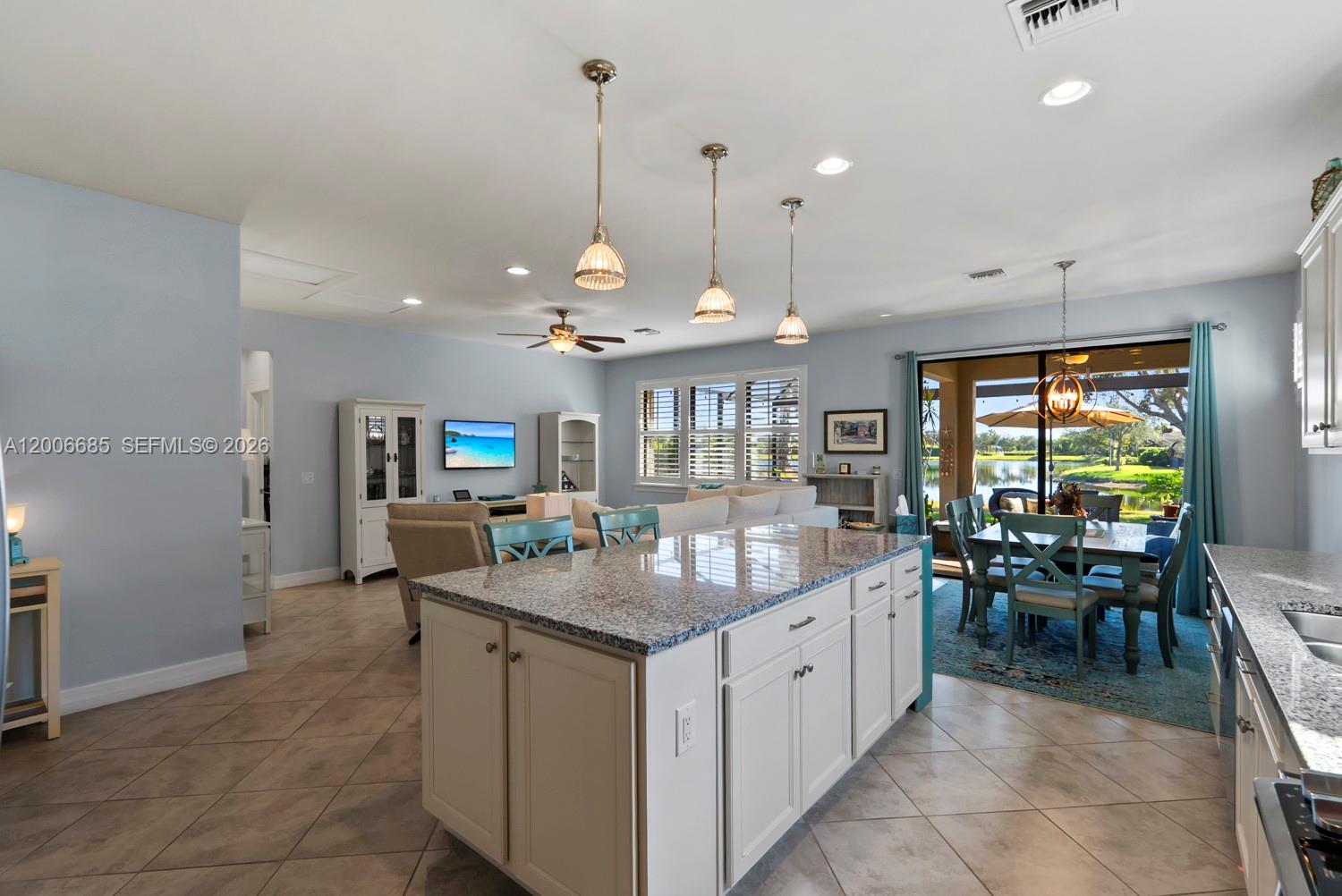 A kitchen with a granite island and white cabinets opens into a living and dining area — 6264 Victory Dr, Ave Maria FL 34142, AVE MARIA, FL