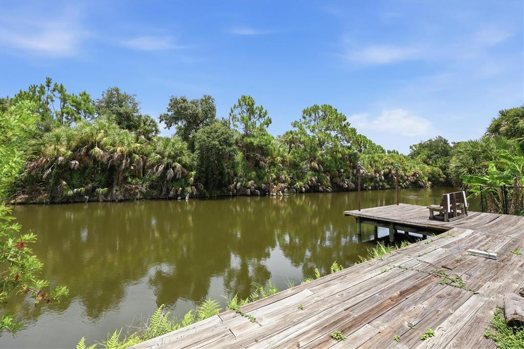 A wooden dock extends over a calm pond surrounded by lush trees and vegetation — 9084 PROSPECT AVENUE, ENGLEWOOD, FL