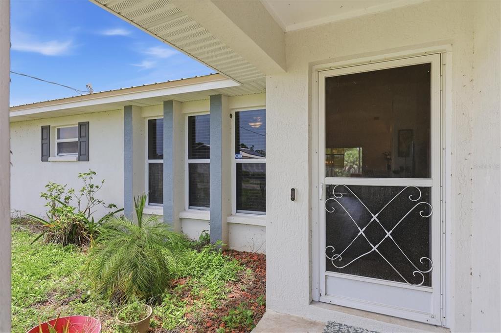 A white house exterior features a covered entryway with a screen door and windows — 9084 PROSPECT AVENUE, ENGLEWOOD, FL