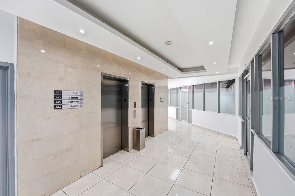 A commercial hallway features two elevators, tiled floors, and a directory sign on a marble wall — 644 FERNANDEZ JUNCOS, SAN JUAN, PR