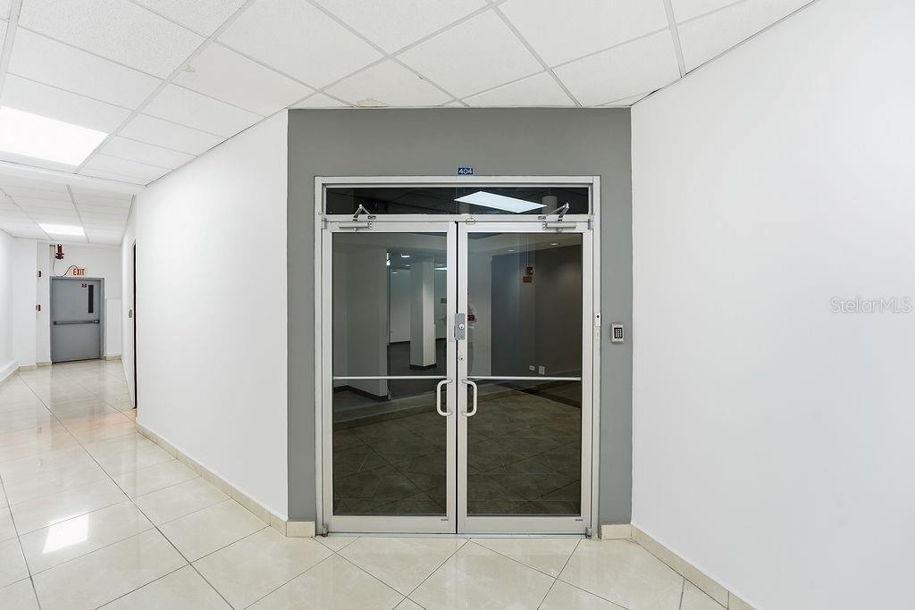 A hallway with white tile floors leads to a glass double door labeled 404 — 644 FERNANDEZ JUNCOS, SAN JUAN, PR