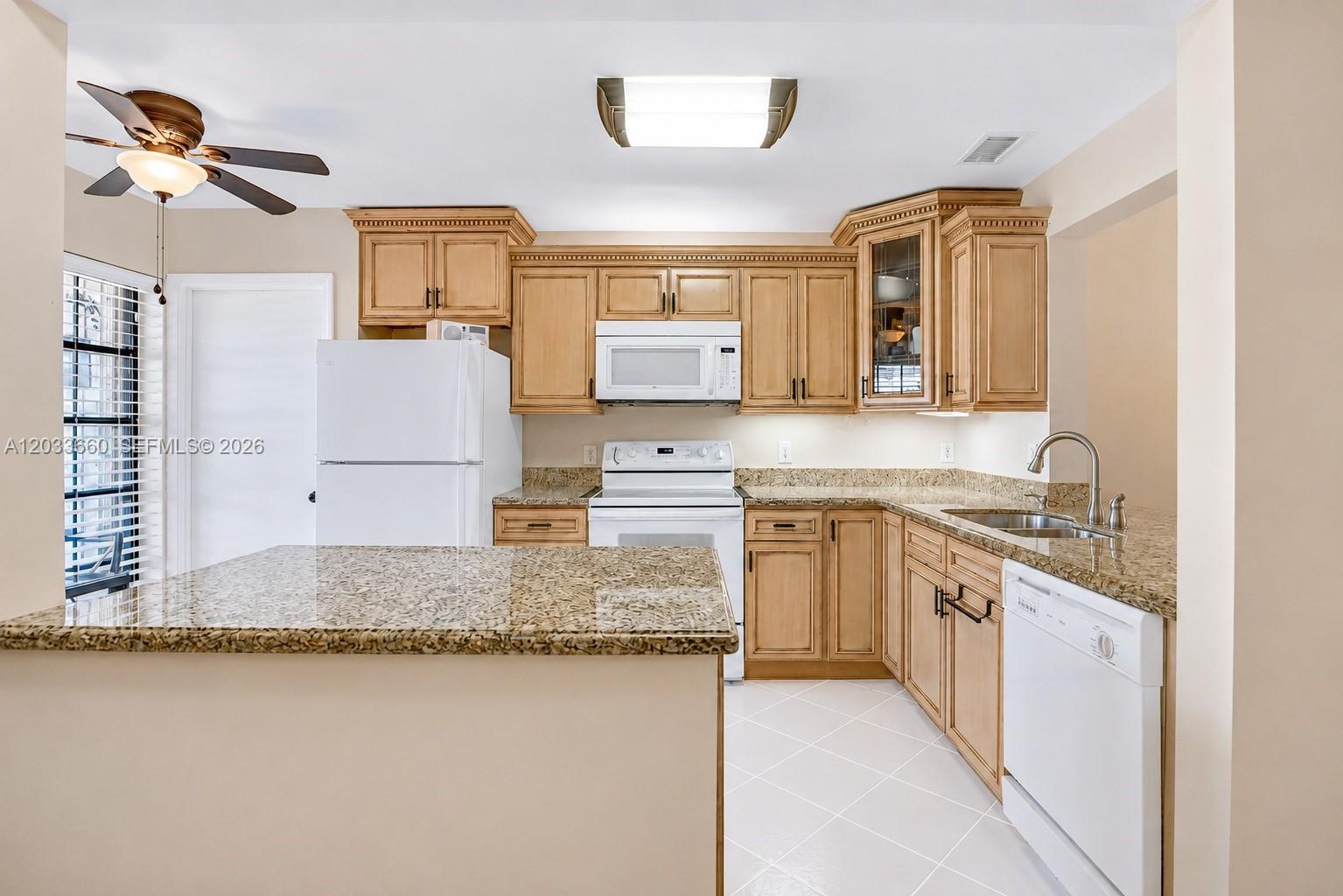A kitchen features light wood cabinets, granite countertops, white appliances, and a tiled floor — 1726 SW 20th Ter, Deerfield Beach FL 33442, DEERFIELD BEACH, FL