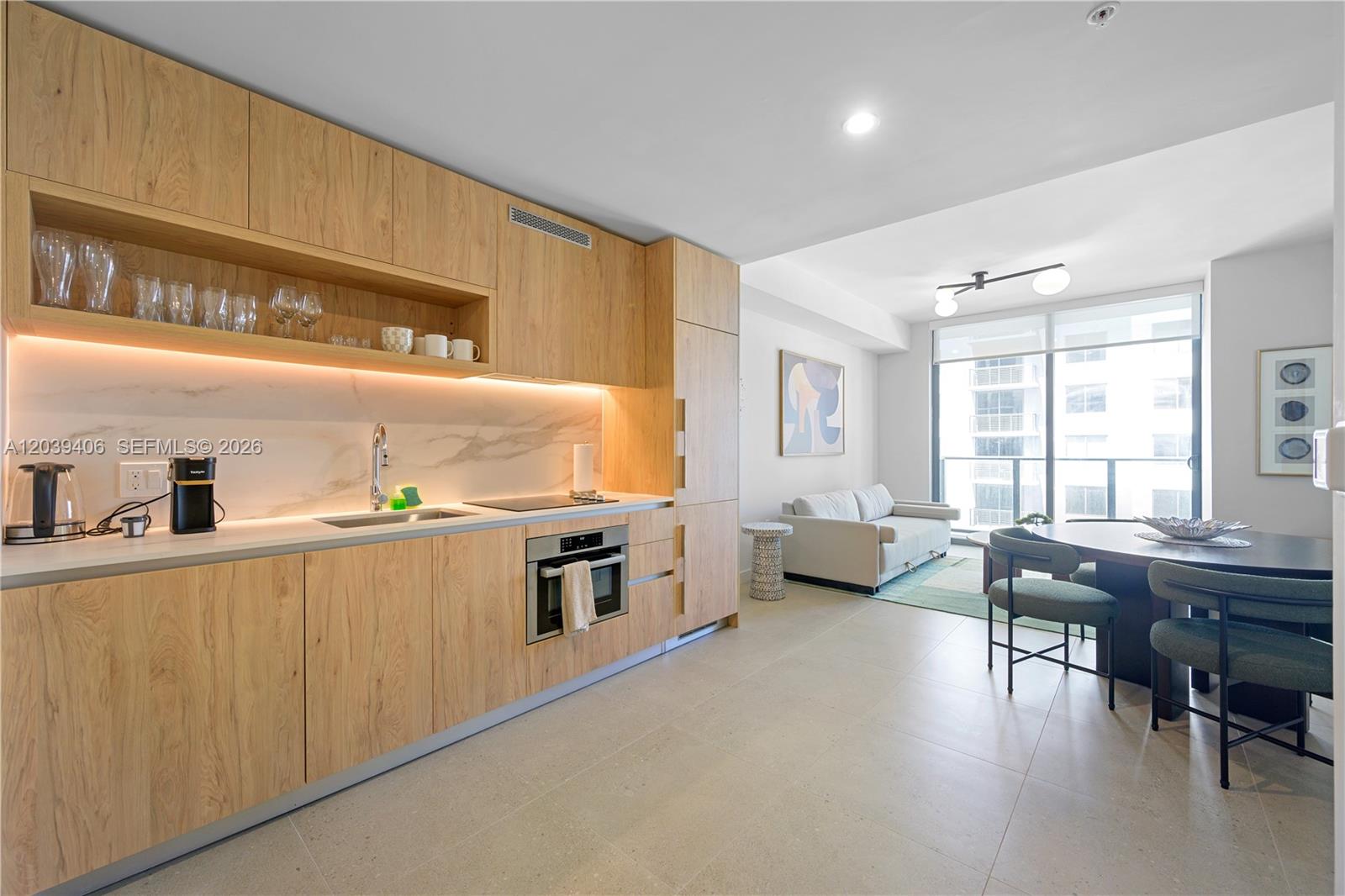 A modern kitchen with light wood cabinetry and marble backsplash opens into a living area — 11 NE 6th St # 2411, Miami FL 33132, MIAMI, FL