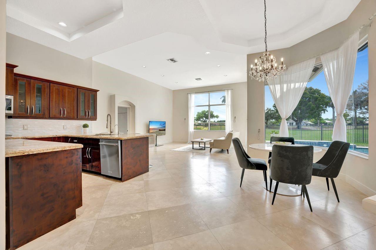 A kitchen with dark wood cabinets and granite countertops opens to a dining and living area — 2491 Eagle Run Drive, Weston FL 33327, WESTON, FL