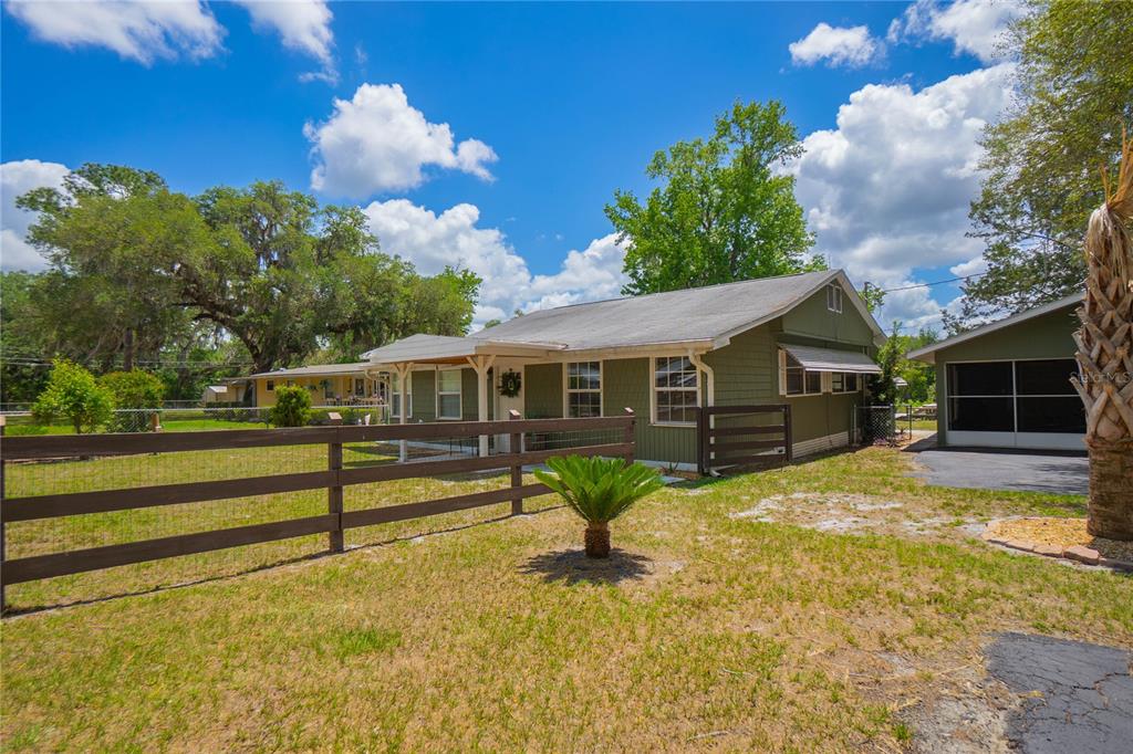 A green, single-story house with a wooden fence and a detached garage under a sky — 4556 E SHOREWOOD DRIVE, HERNANDO, FL