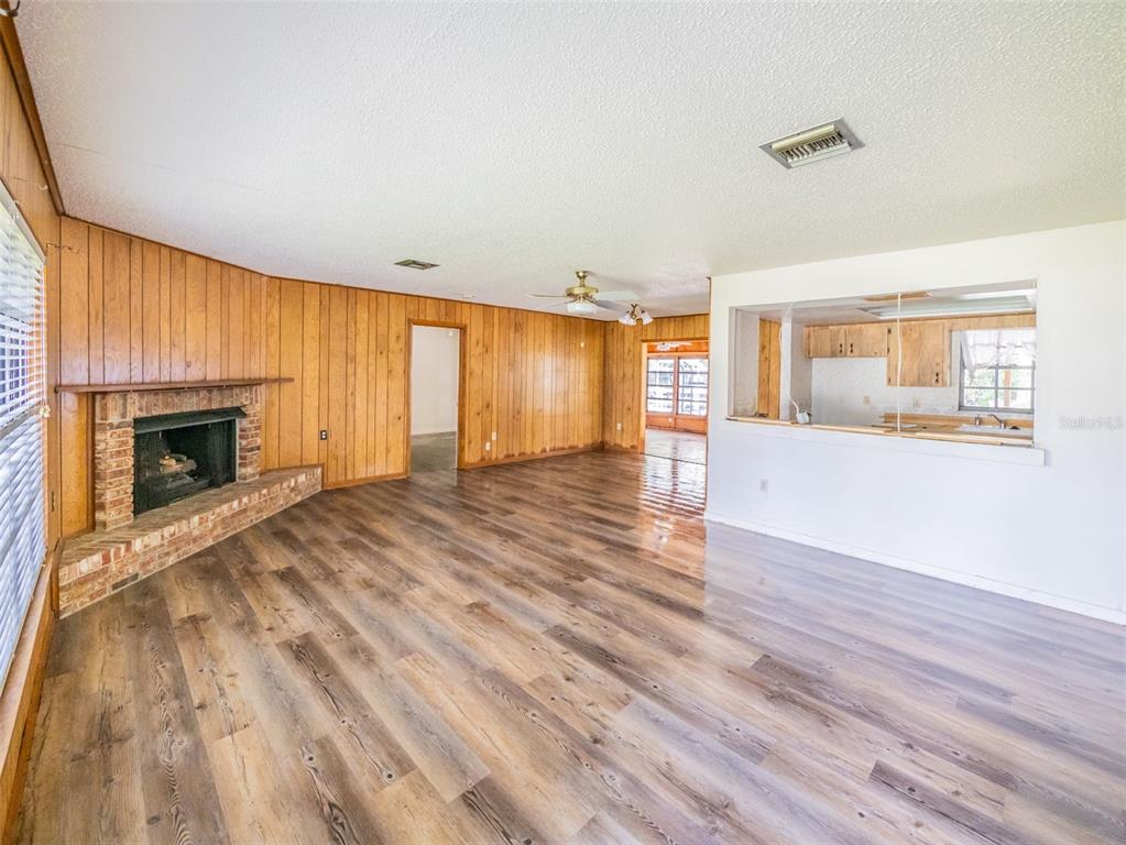 A living room features wood-paneled walls, a brick fireplace, and light-colored wood-look flooring — 55746 CARROL STREET, ASTOR, FL