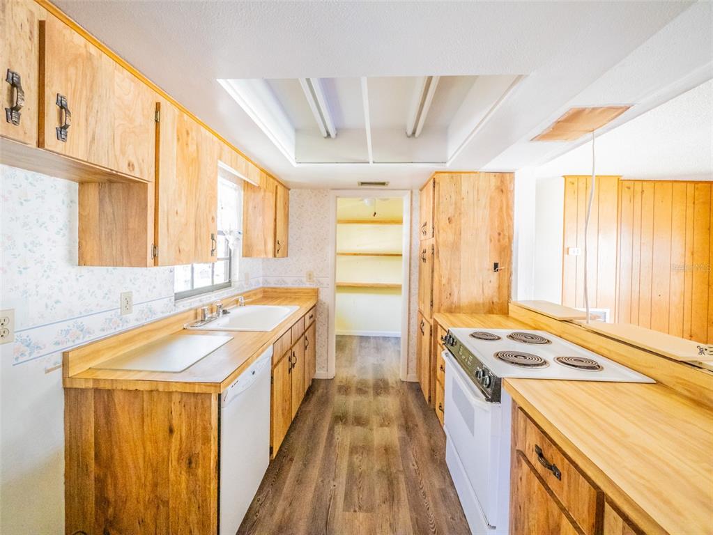 A galley kitchen features wood cabinets, laminate countertops, a white stove, and a pantry doorway — 55746 CARROL STREET, ASTOR, FL