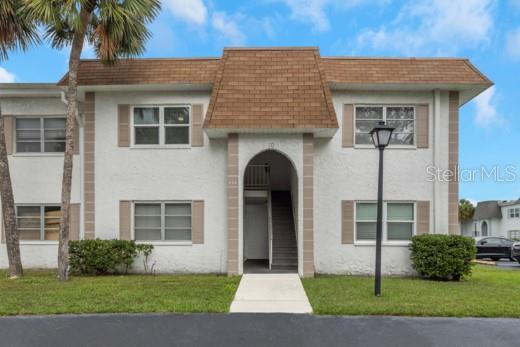 A two-story apartment building features a brown shingled roof, white stucco walls, and a central entryway — 359 S MCMULLEN BOOTH ROAD UNIT 122, CLEARWATER, FL