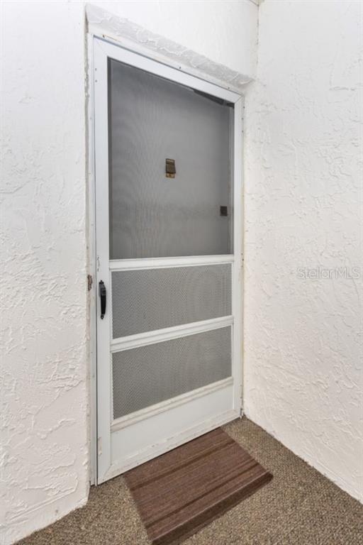 A white storm door with a screen and metal kick plates stands against a textured wall — 359 S MCMULLEN BOOTH ROAD UNIT 122, CLEARWATER, FL