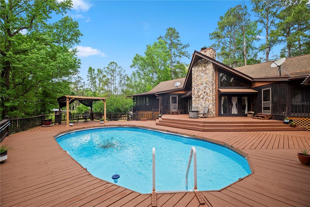 A wooden deck surrounds an oval swimming pool next to a house with a stone chimney — 6967 SHARRON ROAD, GREEN COVE SPRINGS, FL