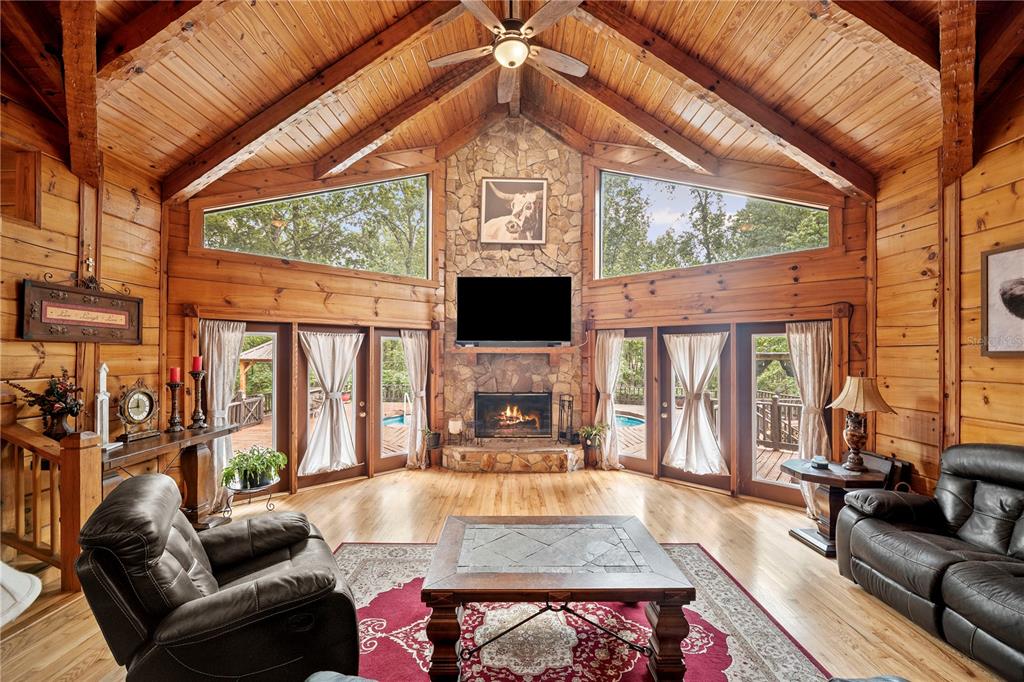 A rustic living room features a stone fireplace, vaulted wood ceilings, and large glass doors — 6967 SHARRON ROAD, GREEN COVE SPRINGS, FL