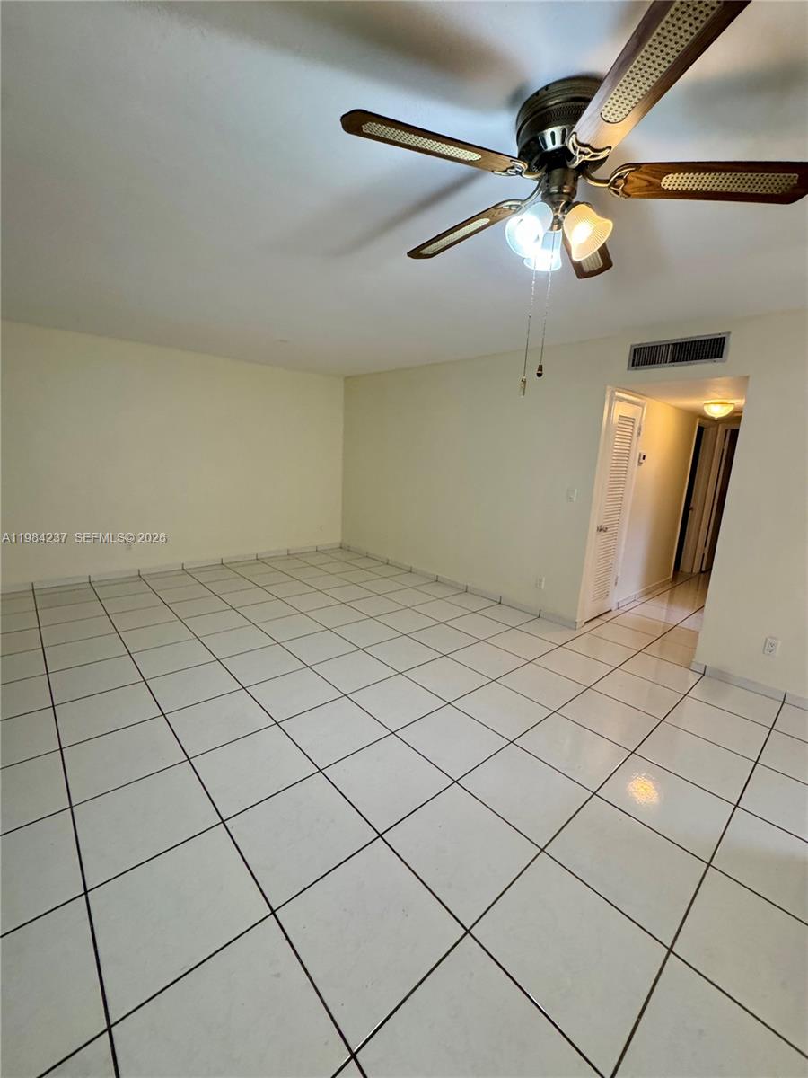 An empty room features white tile flooring, a ceiling fan, and a doorway leading down a hallway — 11234 SW 169th St # V3443, Miami FL 33157, MIAMI, FL