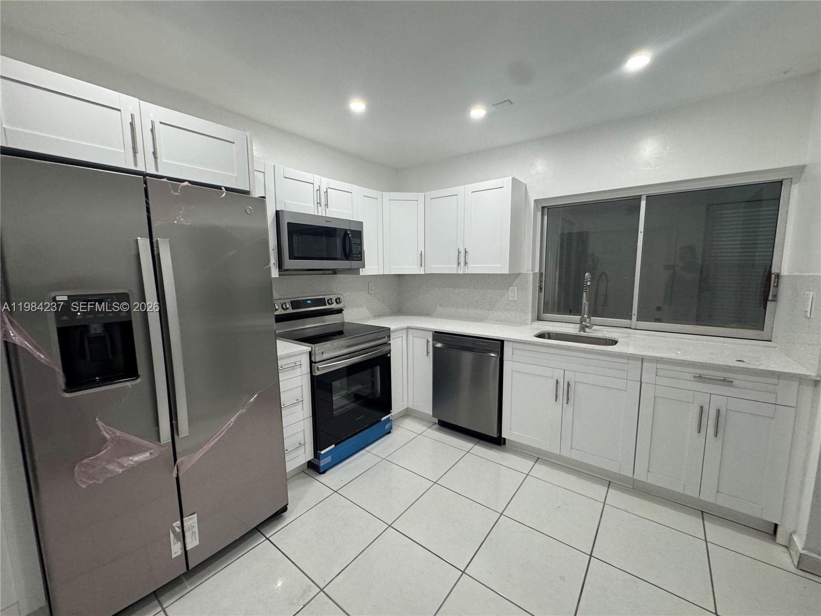 A kitchen features white cabinets, stainless steel appliances, light countertops, and white tile flooring — 11234 SW 169th St # V3443, Miami FL 33157, MIAMI, FL