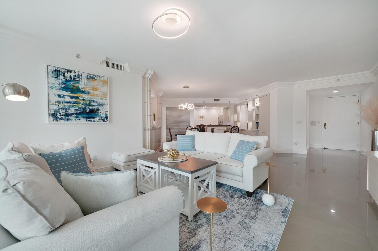 A bright living room features white furniture, a blue patterned rug, and a modern light fixture — 550 SE Mizner Boulevard # B209, Boca Raton FL 33432, BOCA RATON, FL