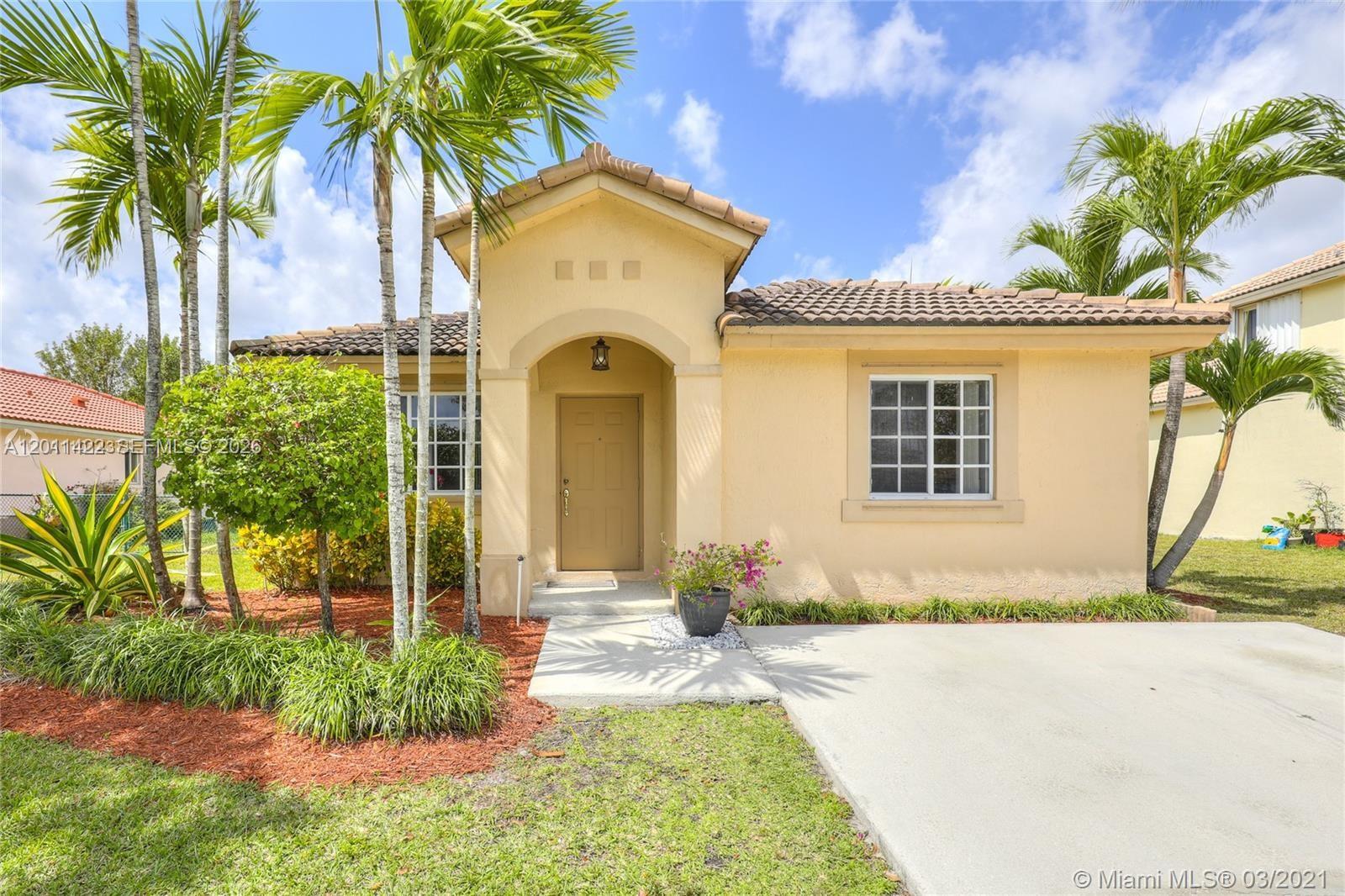A single-story tan stucco house features a tiled roof, palm trees, and a concrete driveway — 450 SE 30th Dr, Homestead FL 33033, HOMESTEAD, FL