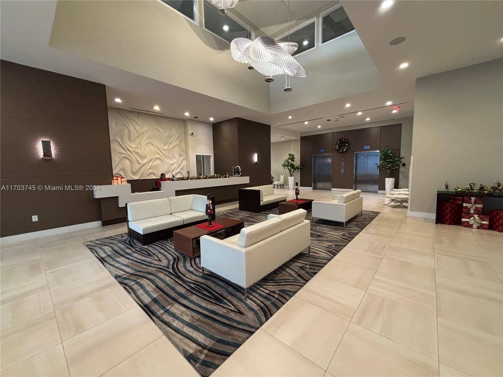 A modern lobby features white sofas, a patterned area rug, and a large sculptural chandelier — 7825 NW 107th Ave # 310, Doral FL 33178, DORAL, FL