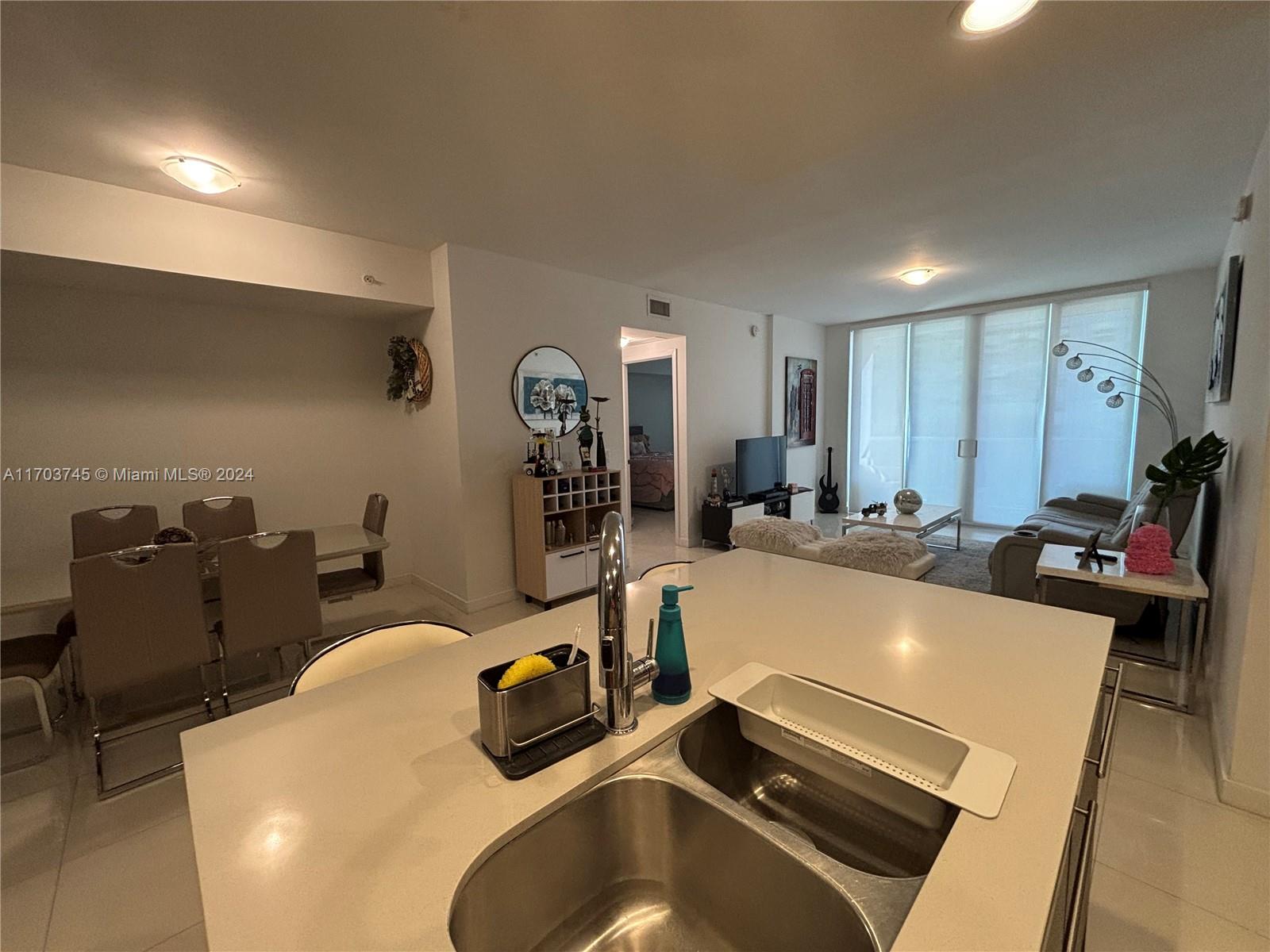 A kitchen island with a double sink overlooks an open-concept living and dining area — 7825 NW 107th Ave # 310, Doral FL 33178, DORAL, FL