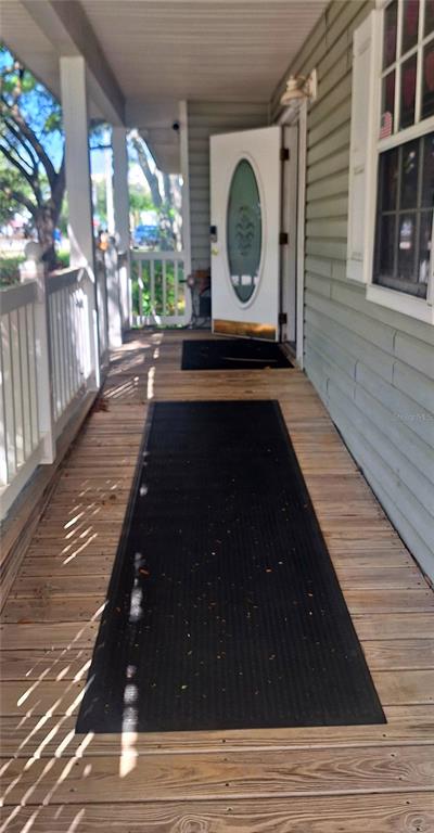 A wooden front porch features a long black mat leading to an open white door — 360 TANGERINE AVENUE, MERRITT ISLAND, FL