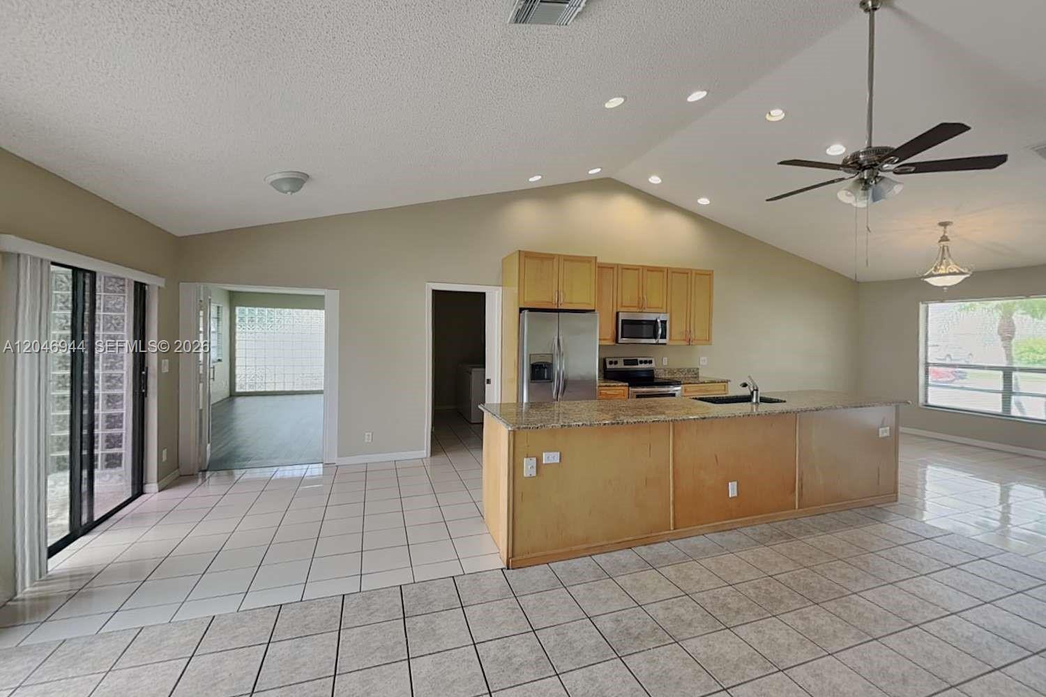 A kitchen with light wood cabinets and a granite island overlooks a tiled living area — BOCA RATON, FL