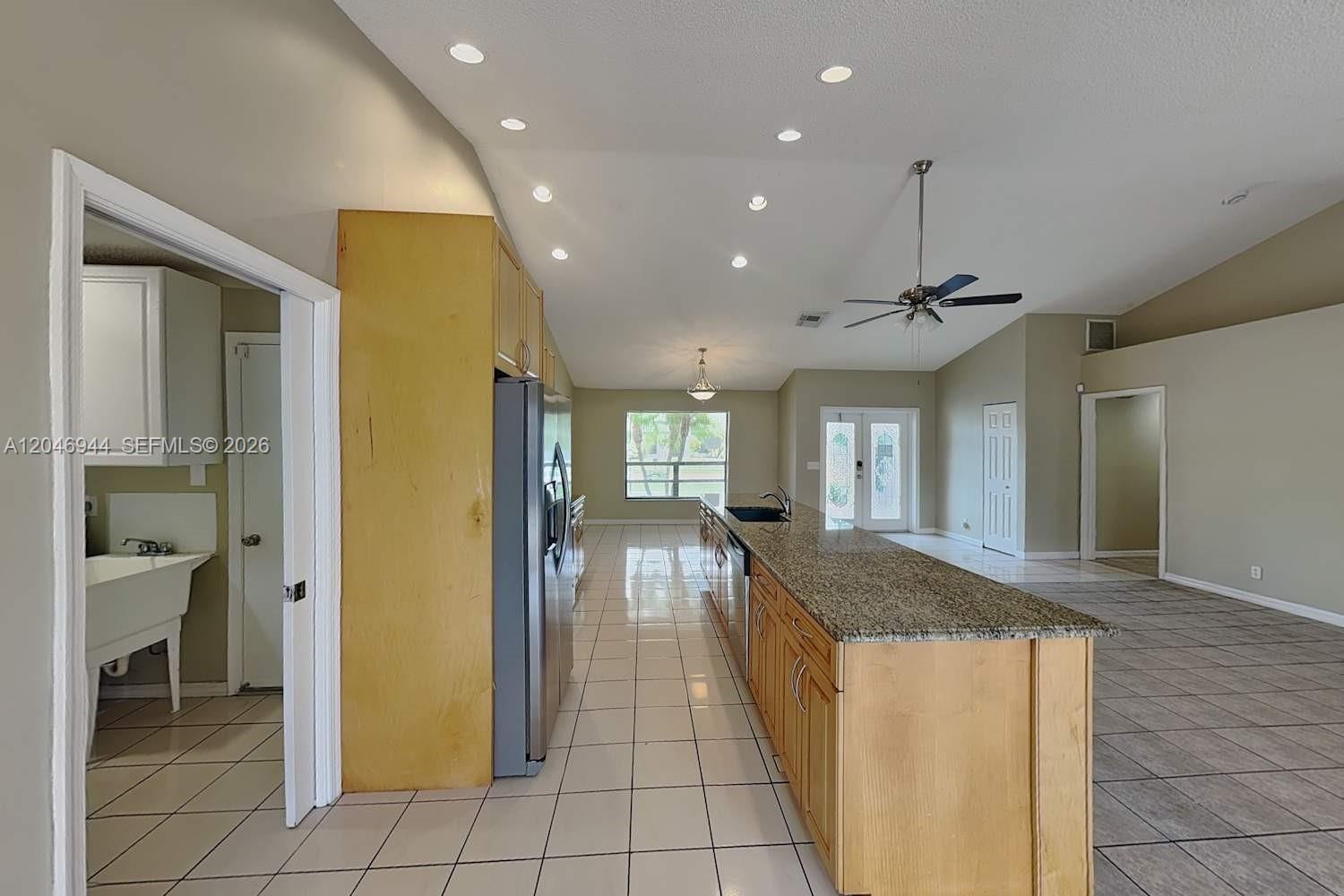 A kitchen with light wood cabinets, granite countertops, and tile flooring opens to a living area — BOCA RATON, FL