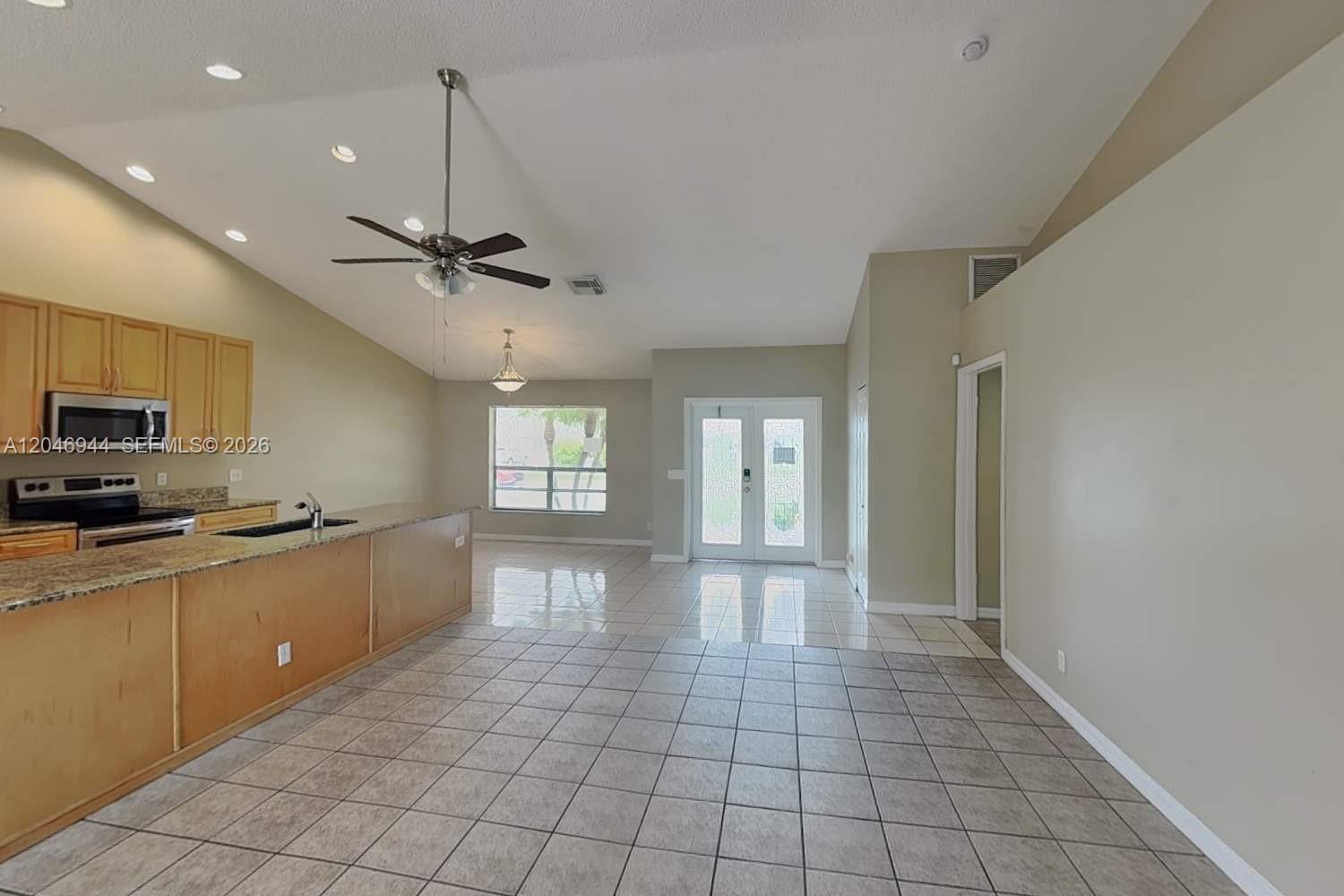 An open-concept kitchen and living area features light wood cabinets, granite countertops, and tile flooring — BOCA RATON, FL