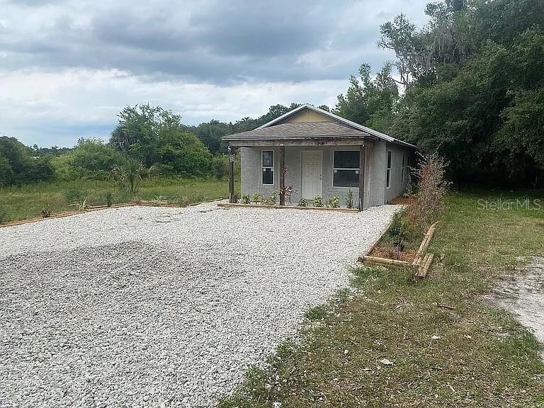 A small, gray, single-story house features a gravel driveway and a covered front porch — 15098 NE 35TH AVENUE ROAD, CITRA, FL