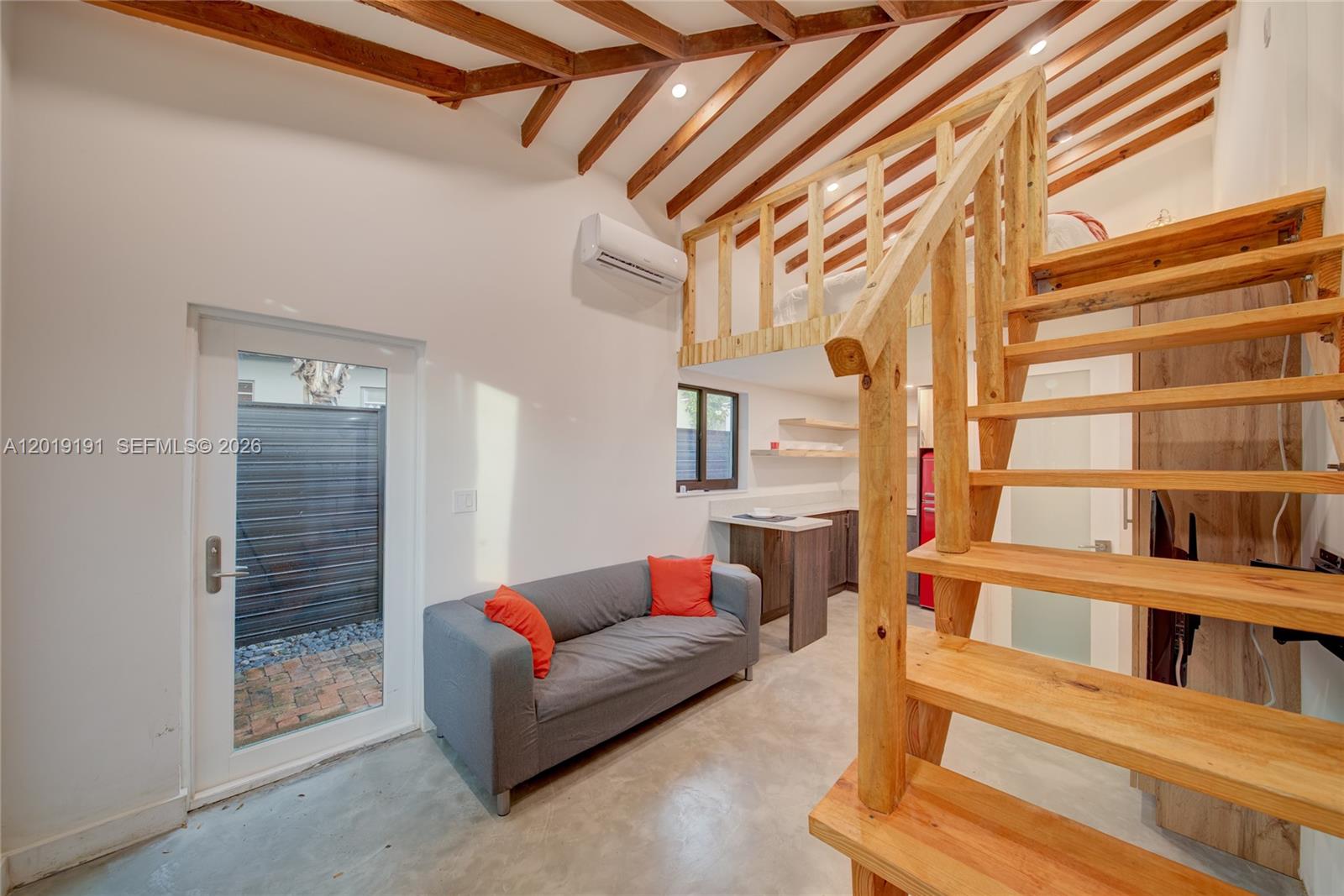 A small living area with a sofa, kitchenette, and wooden staircase leading to a loft — 6631 Tamiami Canal Rd, Miami FL 33126, MIAMI, FL