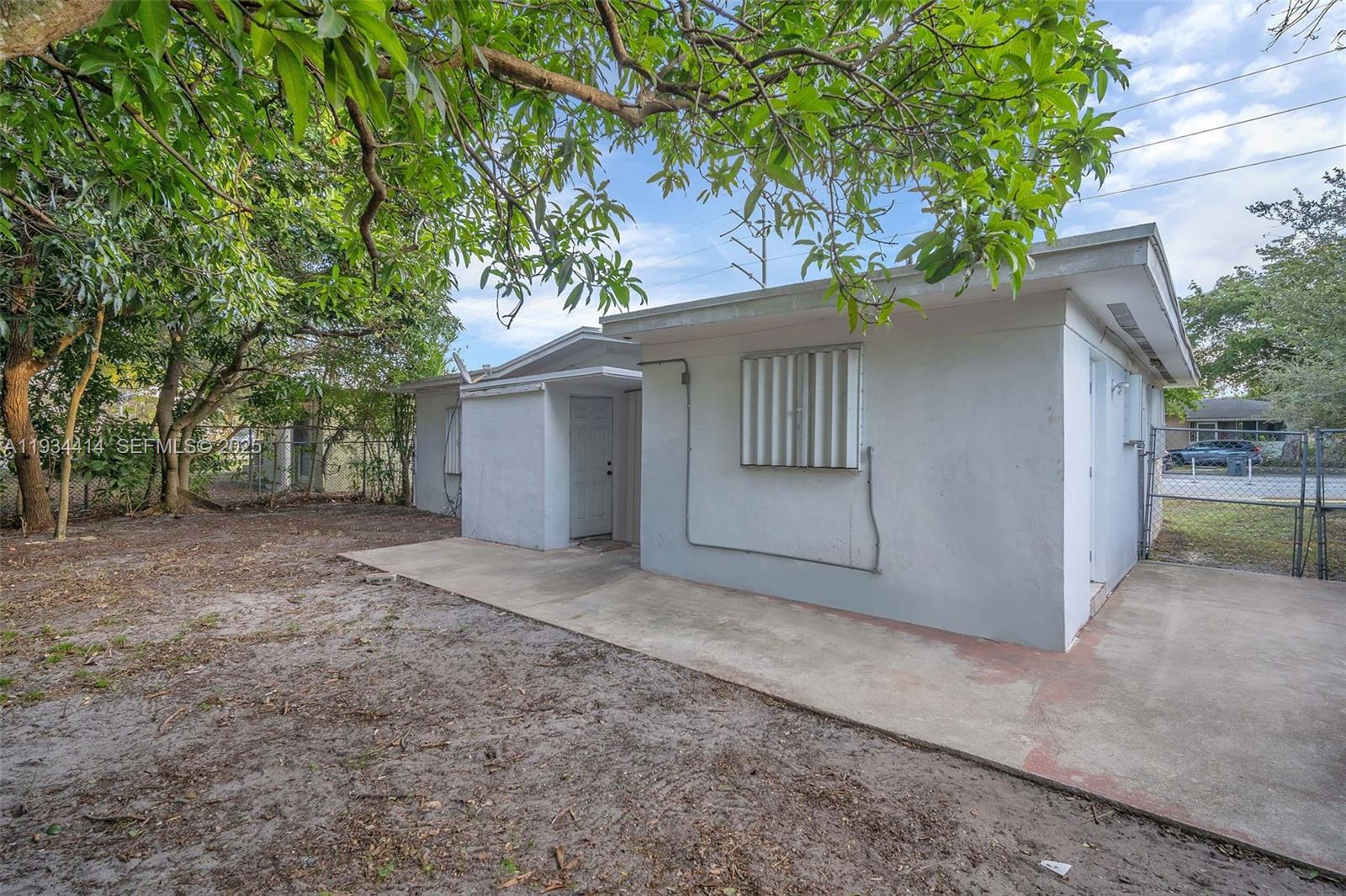 The exterior of a white, single-story house features a concrete patio and a chain-link fence — 265 NW 135th, North Miami FL 33168, NORTH MIAMI, FL