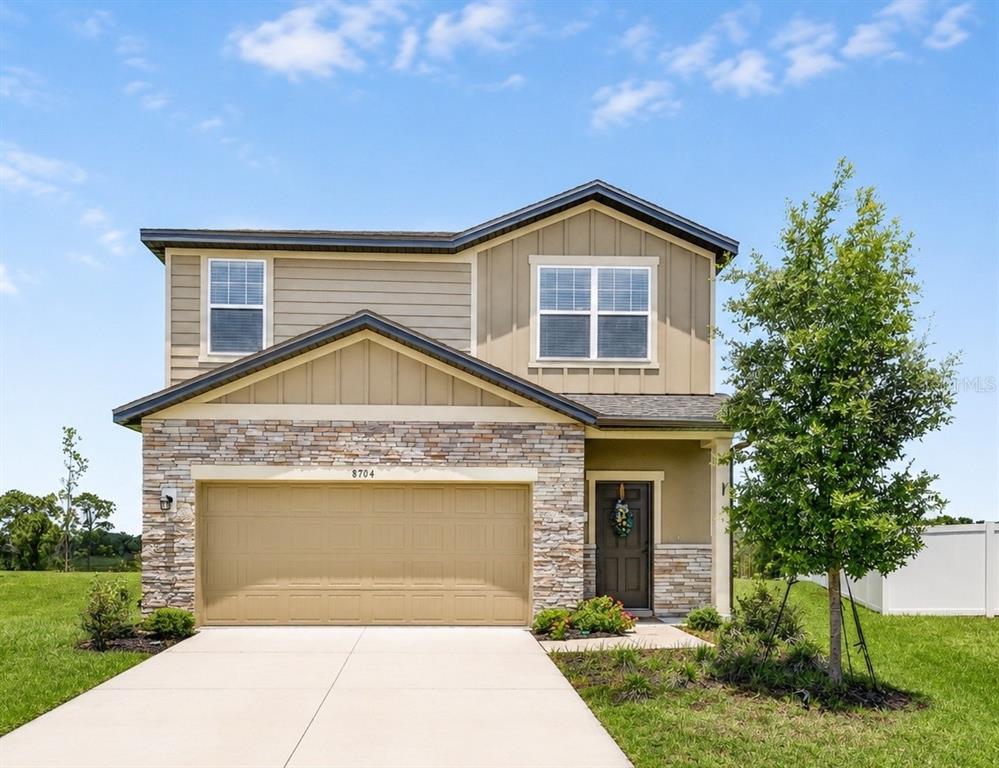 A two-story suburban house features a stone facade, a two-car garage, and tan siding — 8704 SPORTSMAN LOOP, GROVELAND, FL
