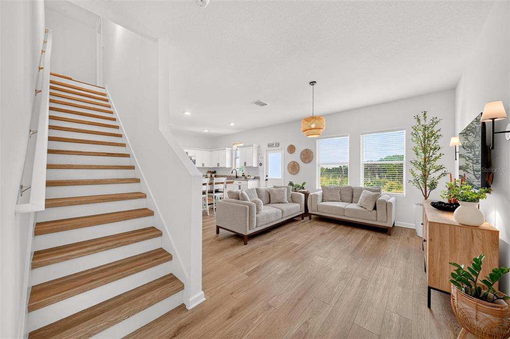 A bright living room features wood-look flooring, two light-colored sofas, and a staircase — 8704 SPORTSMAN LOOP, GROVELAND, FL