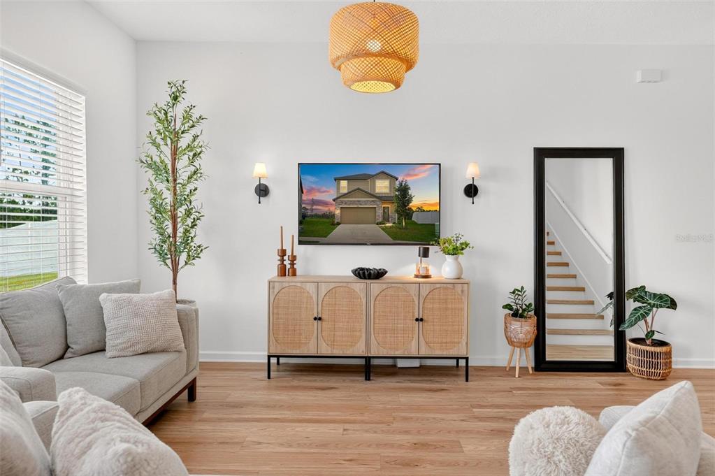 A living room features a television above a wooden cabinet, a mirror, and light flooring — 8704 SPORTSMAN LOOP, GROVELAND, FL