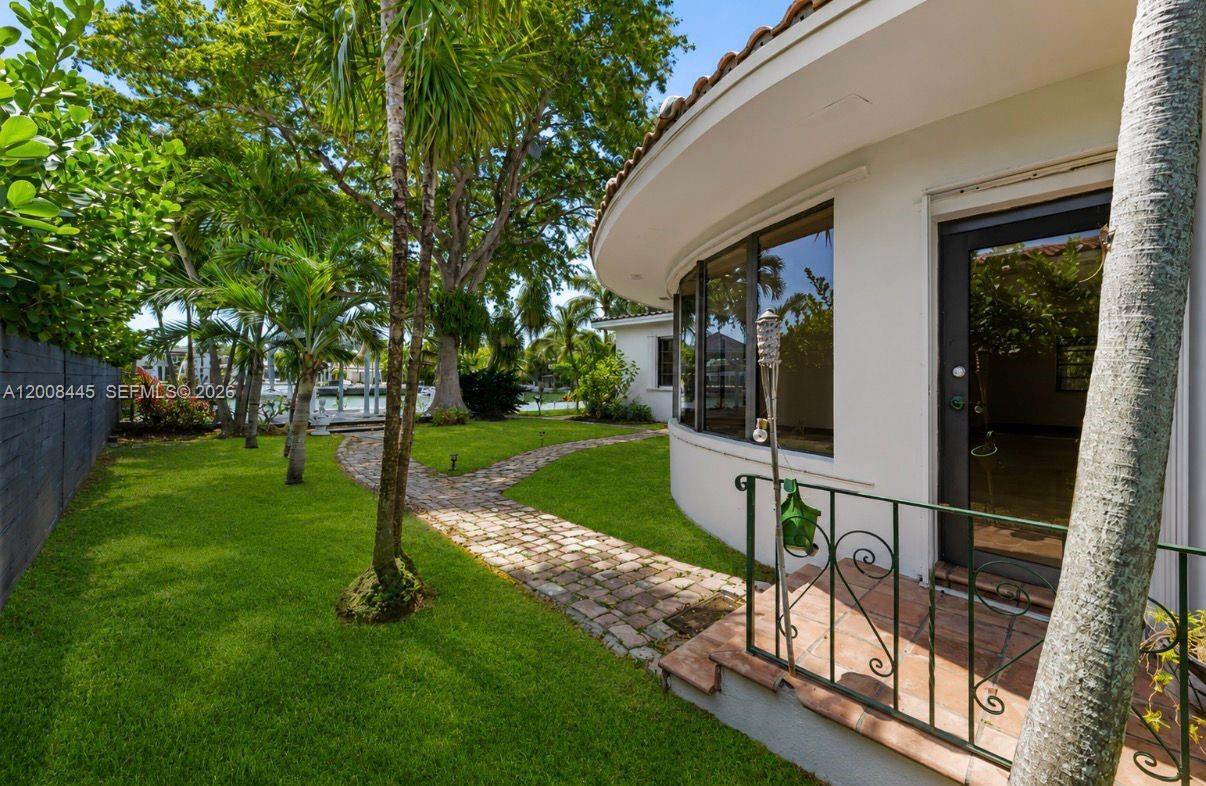 A curved white house exterior features a brick walkway through a grassy backyard with trees — 540 S Shore Dr, Miami Beach FL 33141, MIAMI BEACH, FL