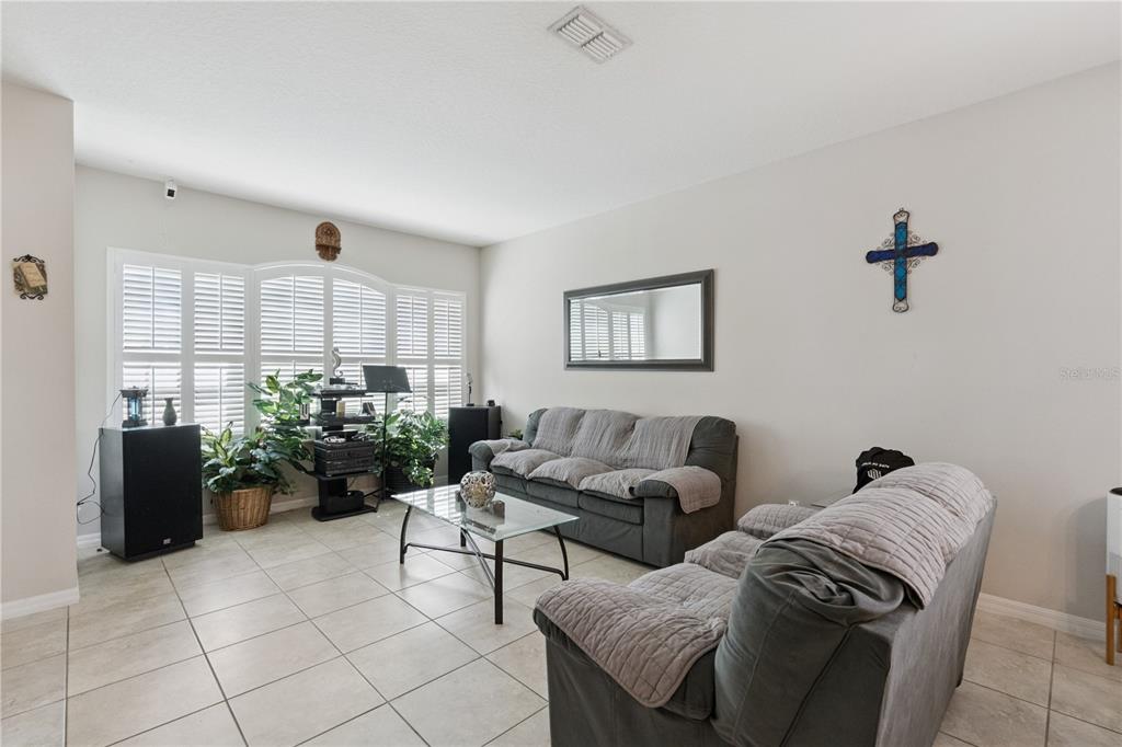 A living room features tile flooring, two gray sofas, a glass coffee table, and shutters — 480 KESTREL DRIVE, GROVELAND, FL