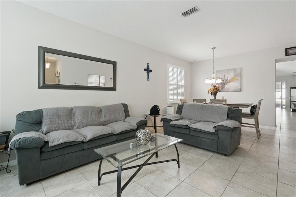 A living room with two gray sofas, a glass coffee table, and an adjacent dining area — 480 KESTREL DRIVE, GROVELAND, FL